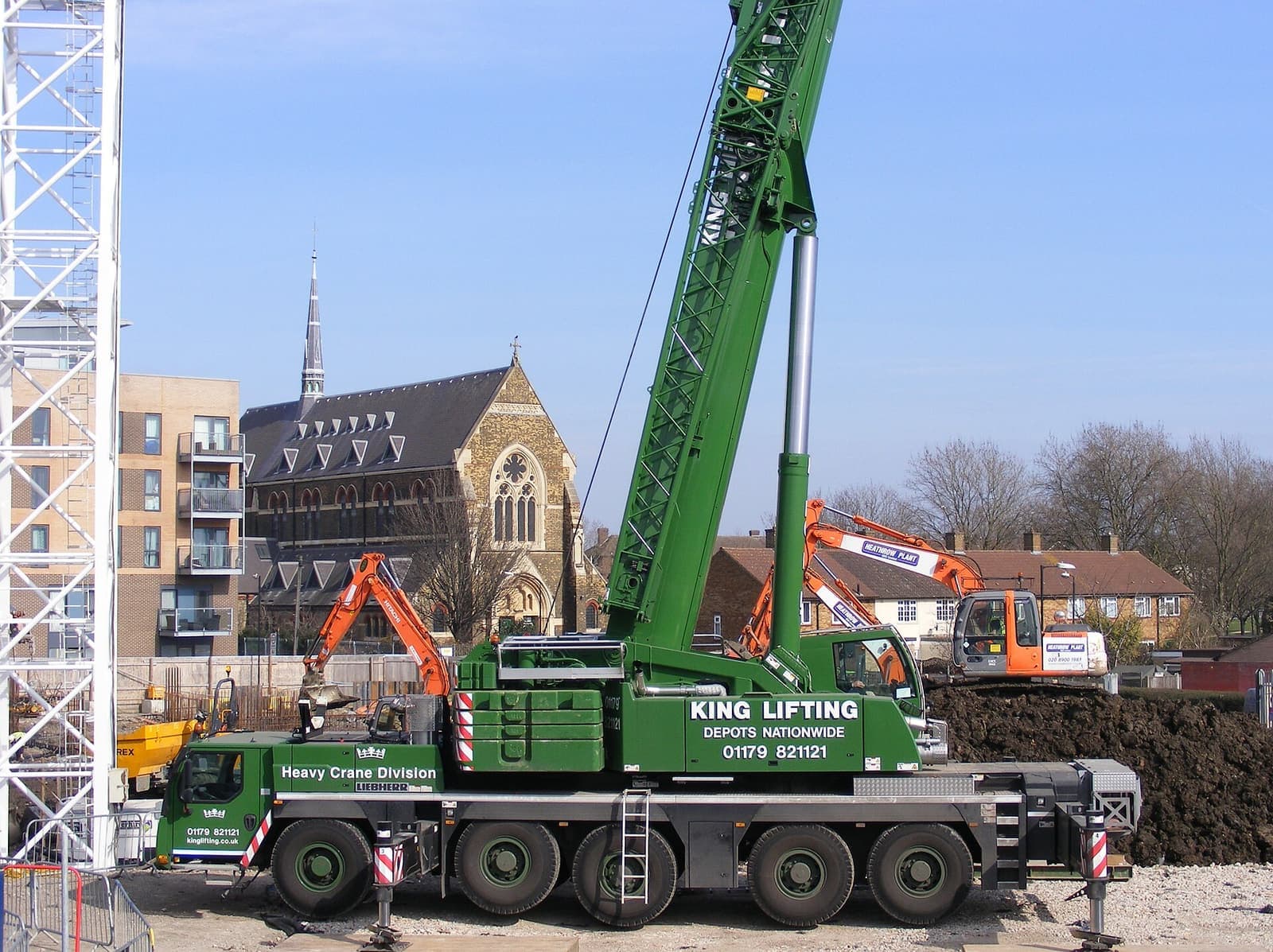 Mobile crane hijau dengan outrigger terpasang di lokasi proyek